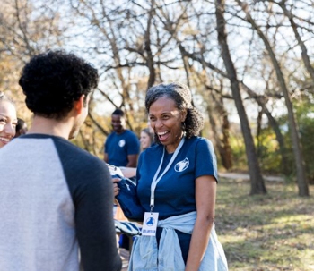 Smiling nurse with lanyard greeting someone outdoors.